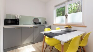 Eine moderne Küche mit grauen Schränken, einer Mikrowelle und einer Kaffeemaschine. Ein Esstisch mit gelben Stühlen und eine Schale Obst am Fensterbrett.
