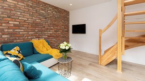 Ein modernes Wohnzimmer mit Backsteinwand, einem blauen Sofa, einer Holztreppe und einem kleinen runden Tisch mit Blumen.