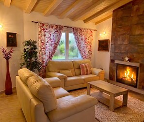 A living room with a sofa, a coffee table, a fireplace, and a window with floral curtains. - Villa 'Dopimar' with Private Pool, Wi-Fi and Air Conditioning (Rincón de la Victoria)