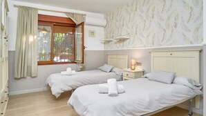 Habitació amb dos llits, una finestra amb cortines, aire condicionat fixat a la paret i una tauleta de nit amb làmpada.