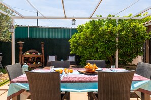 Un patio al aire libre con una mesa dispuesta para comer, rodeado de sillas de mimbre y una pérgola.