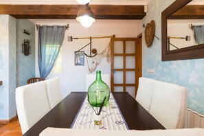 Una mesa de comedor con una botella verde, sillas blancas, techo de madera y una ventana con cortinas.
