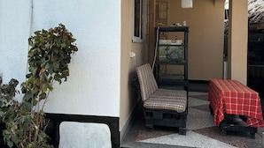 A covered outdoor seating area with a bench, a table with a plaid tablecloth, and a potted plant. - Karibu nest hostel (Dar es Salaam)