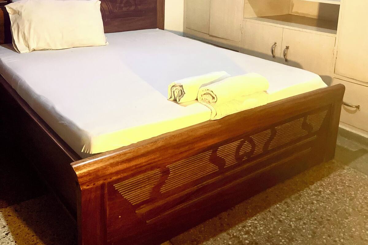 Une chambre à coucher avec un lit en bois, un matelas blanc, un rideau rose et une armoire blanche avec des étagères ouvertes.