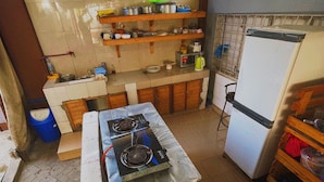 A compact kitchen with a gas stove, a refrigerator, and wooden shelves. - Karibu nest hostel (Dar es Salaam)
