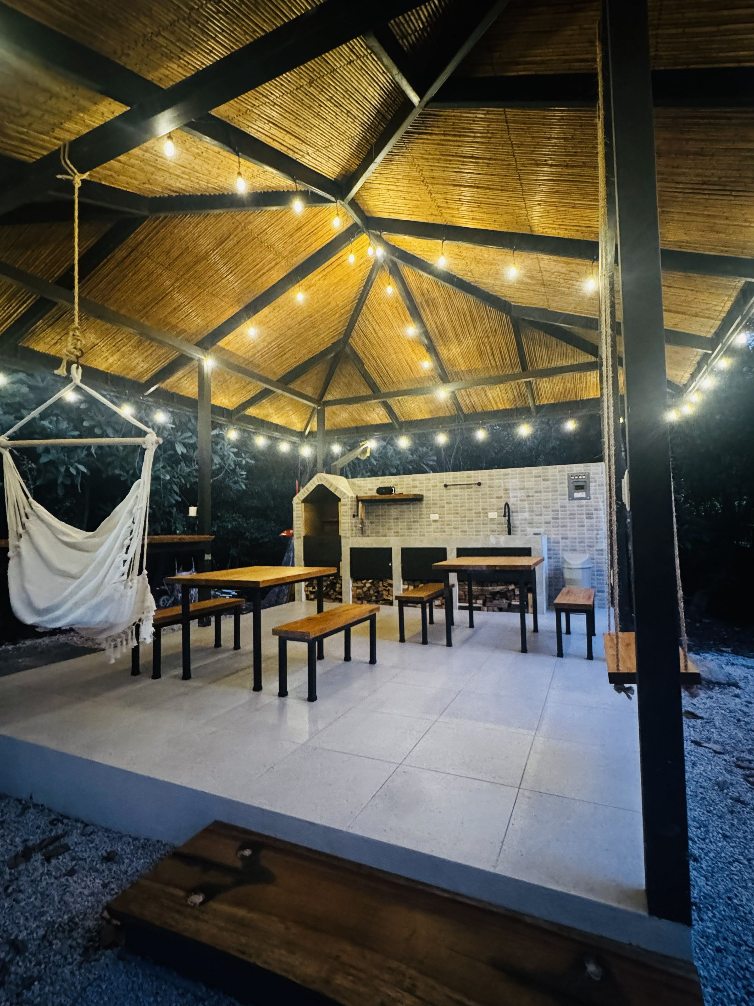 Un espace de restauration en plein air doté d’un toit de chaume, de guirlandes lumineuses et d’un mur de briques avec un évier.