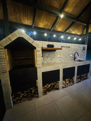Una cocina al aire libre con horno de ladrillo, pileta y espacio integrado para guardar leña.