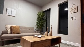 Ett modernt vardagsrum med ett träbord, en grå soffa, en krukväxt och ett stort fönster.