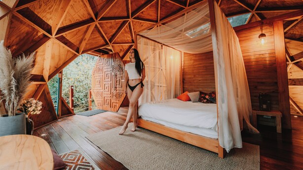 A wooden cabin with a bed, a small table, and a potted plant. - Ráquira Glamping (Ráquira)