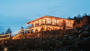 A large, well-lit building with multiple levels and a balcony, surrounded by rocks and trees. - Ráquira Glamping (Ráquira)
