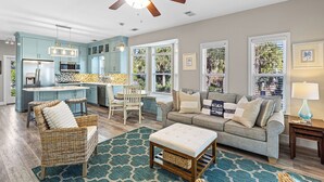 A spacious living area with a kitchen, a dining table, a sofa, and a ceiling fan. - Redfish Cottage - Old Florida Cottages, Community Pool, Easy Walk to the Beach! (Old Florida Cottages)