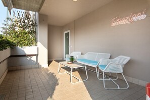 Un balcone con zona salotto esterna in bianco, una pianta in vaso e un cartello attaccato al muro.