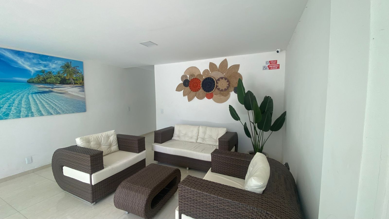 A living room with a large painting of a beach, a wall-mounted flower decoration, and a potted plant.