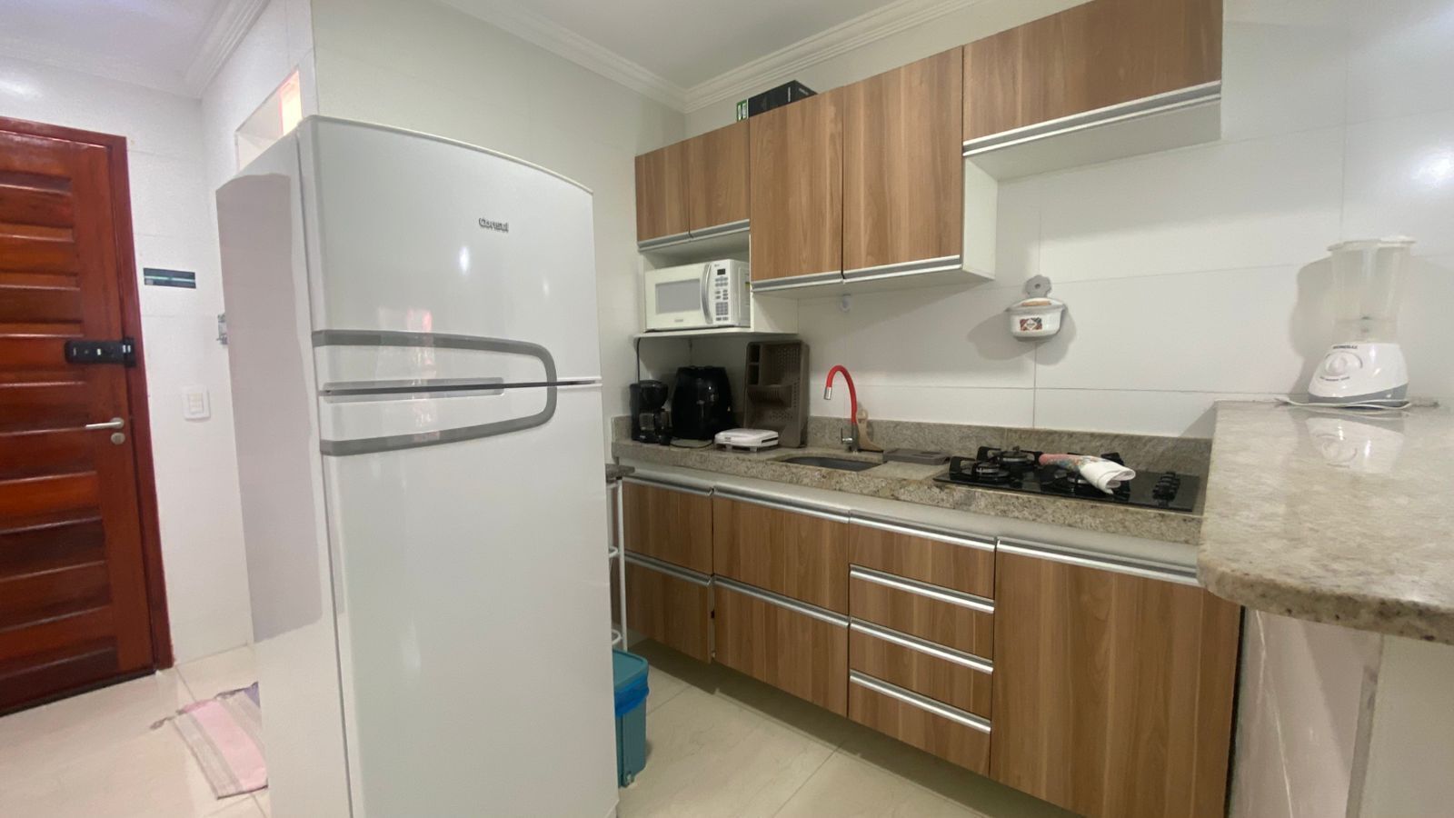 A kitchen with a white refrigerator, wooden cabinets, a microwave, a coffee maker, and a sink with a red faucet.