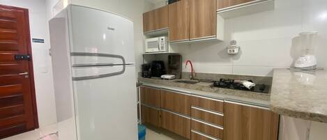 A kitchen with a white refrigerator, wooden cabinets, a microwave, a coffee maker, and a sink with a red faucet.