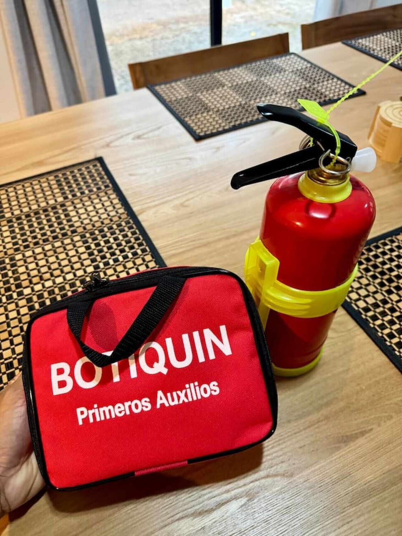 A red fire extinguisher and a red bag with 'BOTTQUIN Primeros Auxilios' text on a table.