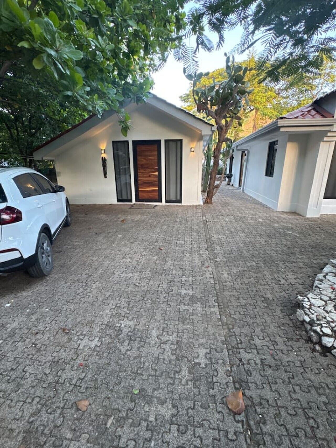 A modern house with a paved driveway, a white car parked in front, and a tree in the center.