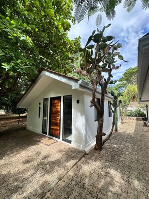 A small, single-story building with a white exterior, a wooden door, and a small patio area. - Private 1BR Retreat | Pool | Playas Del Coco (Coco)