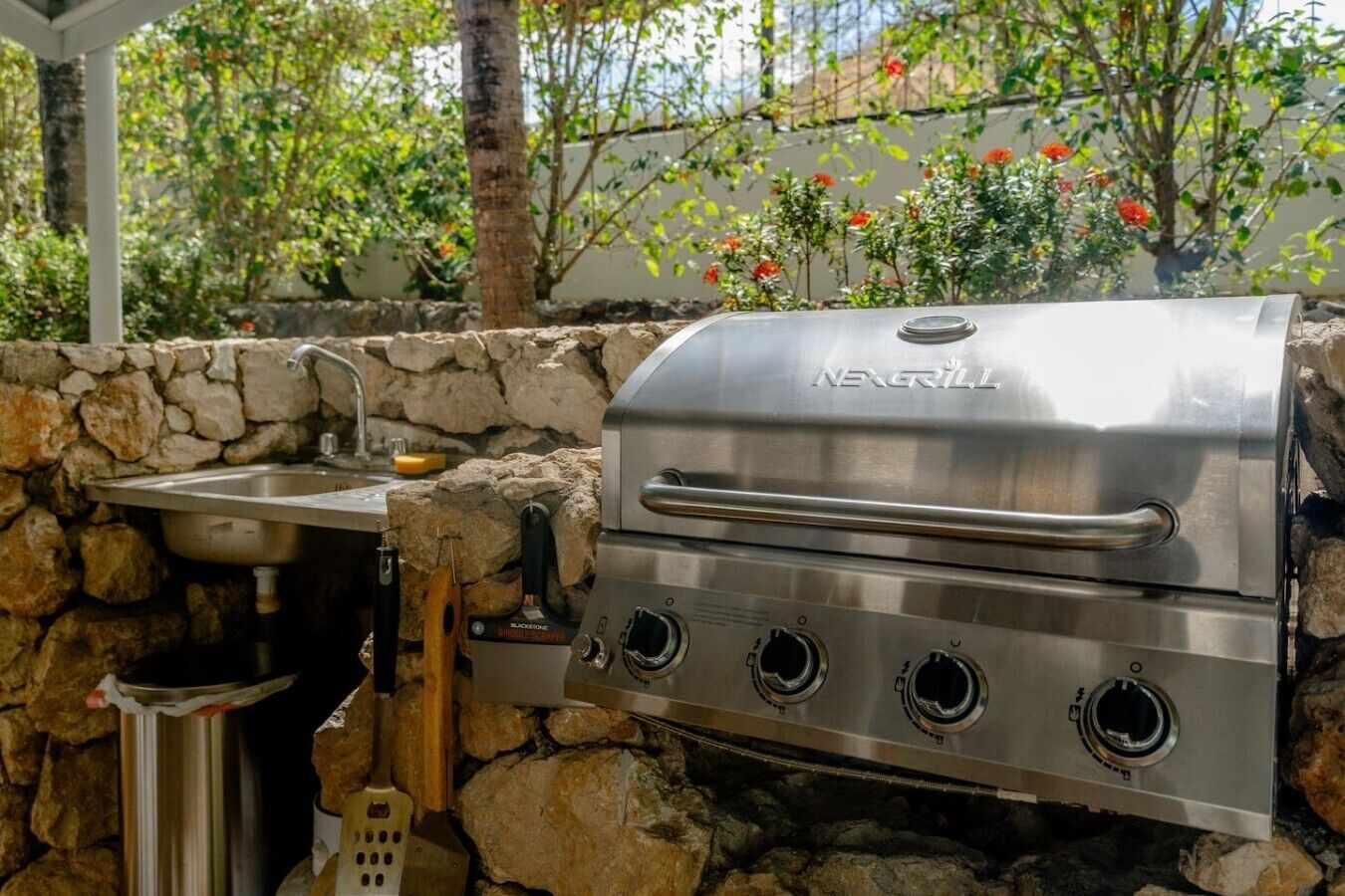 A stainless steel grill with a handle, a sink, and a stone wall.