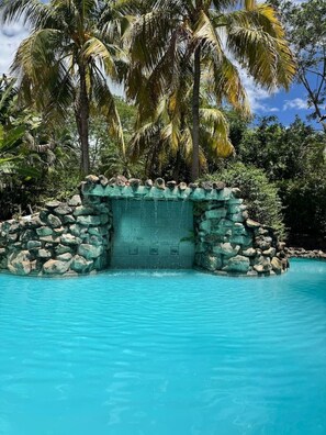 A pool with clear blue water, surrounded by a stone wall and palm trees. - Private 1BR Retreat | Pool | Playas Del Coco (Coco)