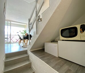 Eine Treppe führt zu einem Essbereich mit Stühlen und einem Tisch. Eine Mikrowelle ist auf der rechten Seite sichtbar.