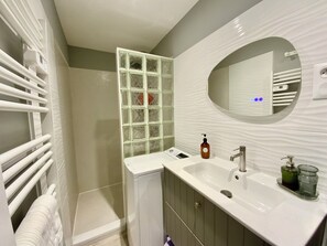 Ein Badezimmer mit einem weißen Waschbecken, einem Spiegel und einer Duschkabine aus Glas.