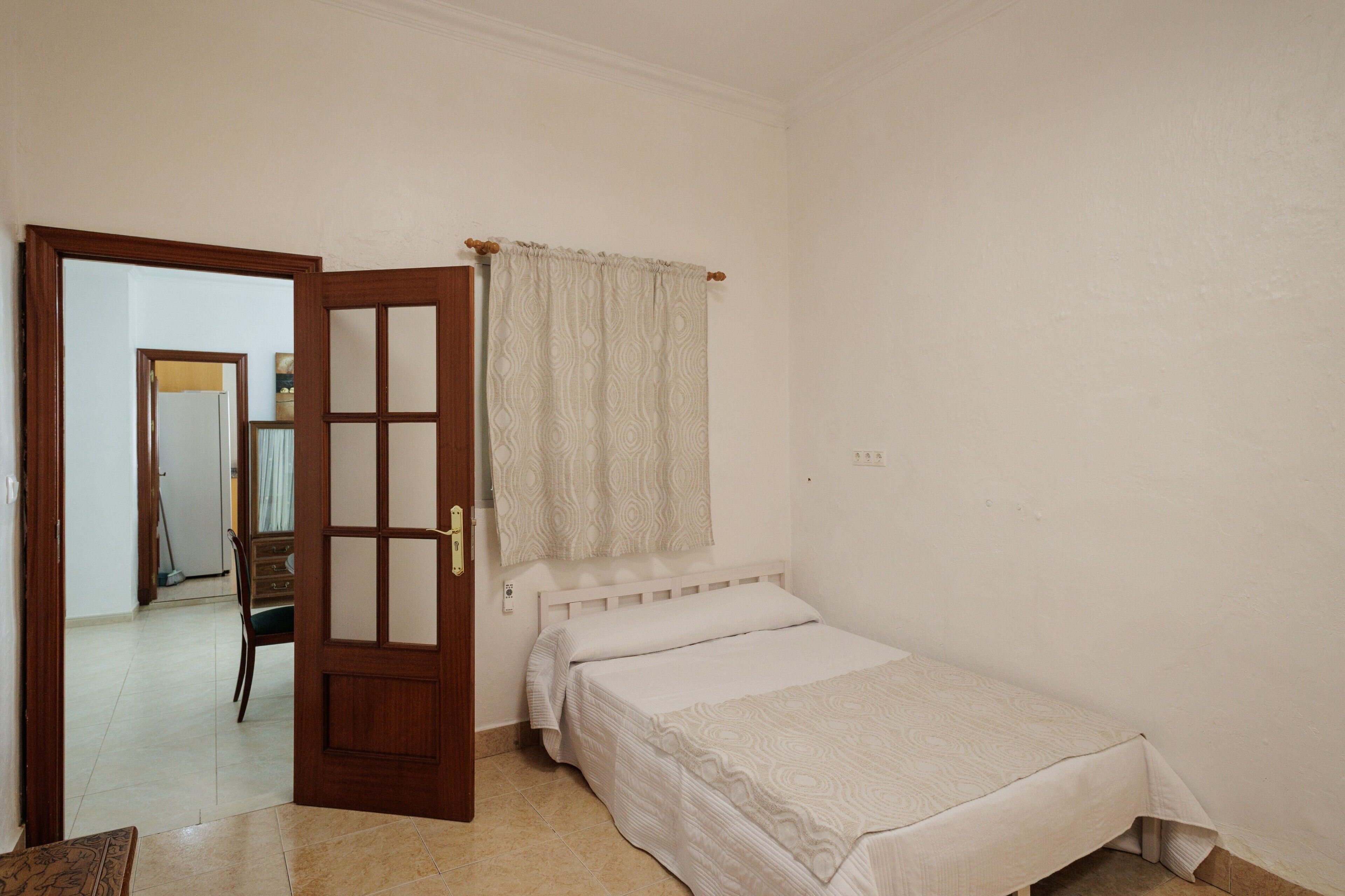 A bedroom with a bed, a door, a mirror, and a chair.