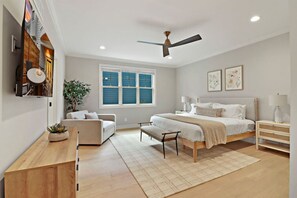 Un dormitorio moderno con una cama, mesitas de noche, ventilador de techo, un ventanal grande y una planta.