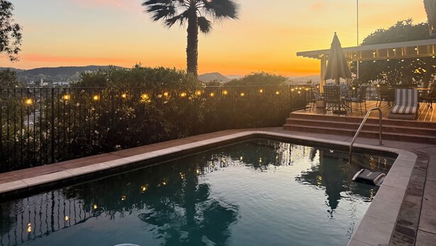 Une piscine avec vue sur un coucher de soleil, des palmiers et un espace salon extérieur.