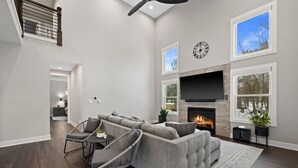 A spacious living room with a fireplace, large windows, and a modern design. - New Luxe Lake Home - Entertainment Rms - Lake view (Lake Geneva)