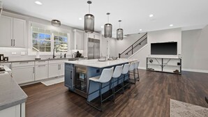 A modern kitchen with white cabinets, a central island with bar stools, stainless steel appliances, and pendant lighting. - New Luxe Lake Home - Entertainment Rms - Lake view (Lake Geneva)