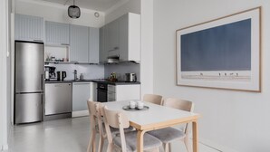 A modern kitchen with stainless steel appliances, a dining area with a white table and chairs, and a framed landscape painting on the wall. - Premium 7th Floor Apartment - Sea View & Historic District (Helsinki)