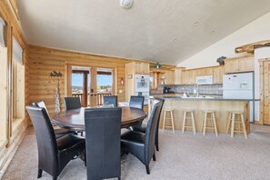 A log cabin with a dining area featuring a round table and chairs, a kitchen with wooden cabinets and modern appliances, and a view through the windows. - Stunning Bear Lake retreat with lake views and games (Garden City)