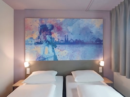 Habitación de hotel con dos camas, un cuadro de paisaje urbano en la pared y vistas al horizonte de la ciudad.