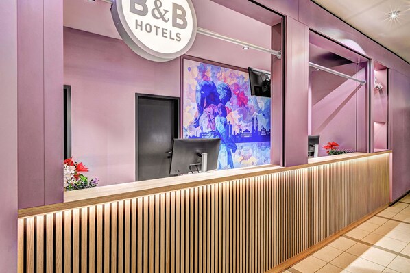 A reception desk with a modern design, a large digital display, and a sign for B&B Hotels. - B&B Hotel Kassel-Wilhelmshöhe (Kassel)
