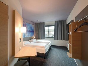 Habitación de hotel con dos camas, un escritorio, un armario y vistas a la ciudad.