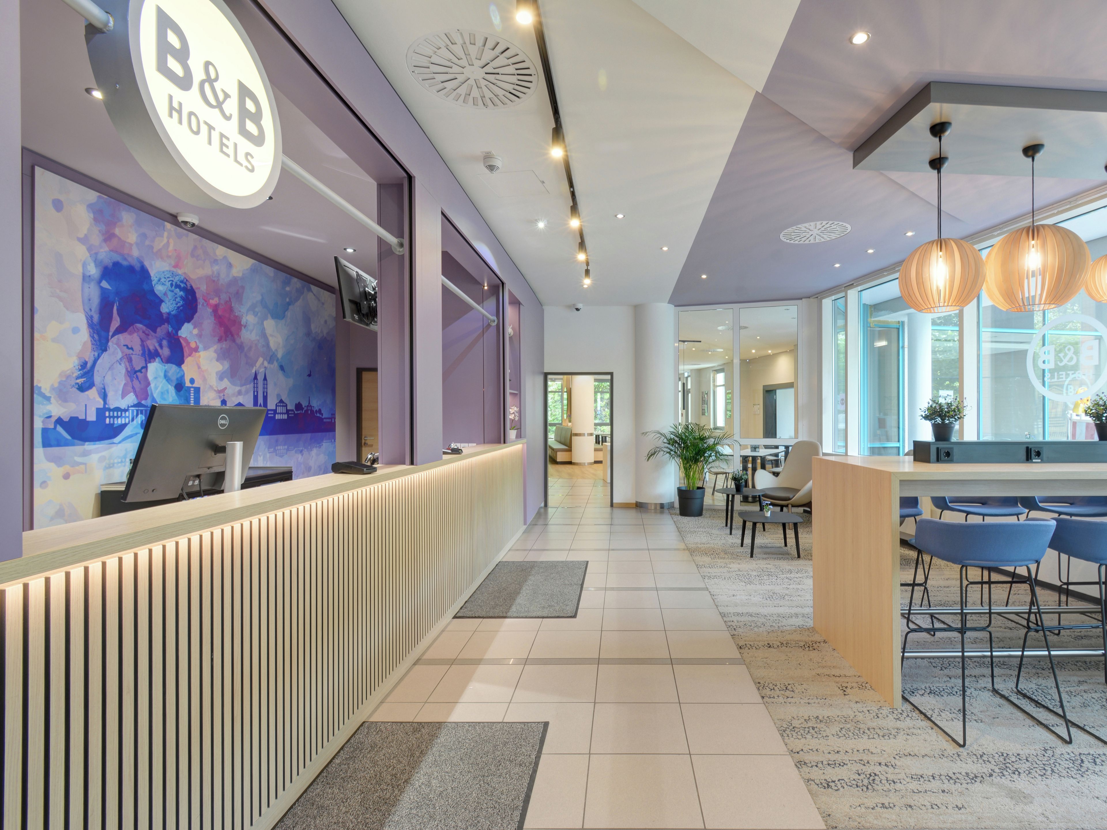Ein Hotel-Empfangsbereich mit modernem Design, inklusive einer Rezeption, eines großen Fensters und einer Sitzecke mit Stühlen.