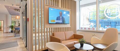 En modern hotellobby med en tv-skärm, en sittgrupp och stora fönster.