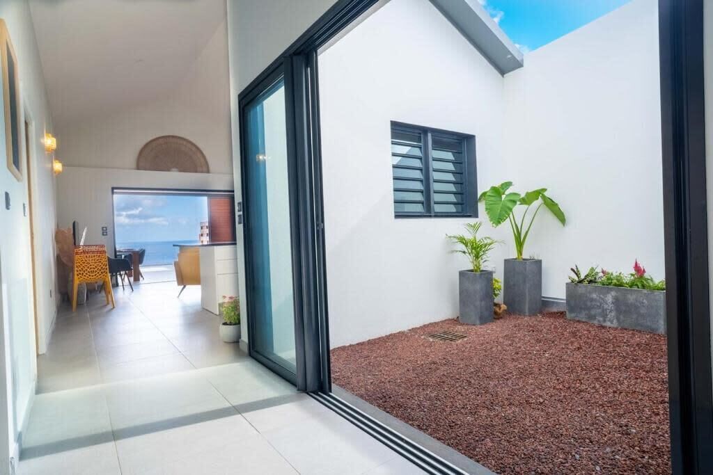 A modern interior with a glass door leading to a balcony, a dining area with a table and chairs, and potted plants.
