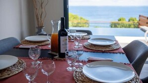 Tavola imbandita con piatti, bicchieri e una bottiglia di vino, con vista su un panorama marino.