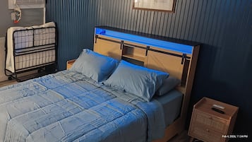 Una cama bien hecha con un edredón azul, un cabecero de madera y una mesita de noche con un control remoto.