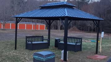 A gazebo with benches and trash bins in a grassy area.