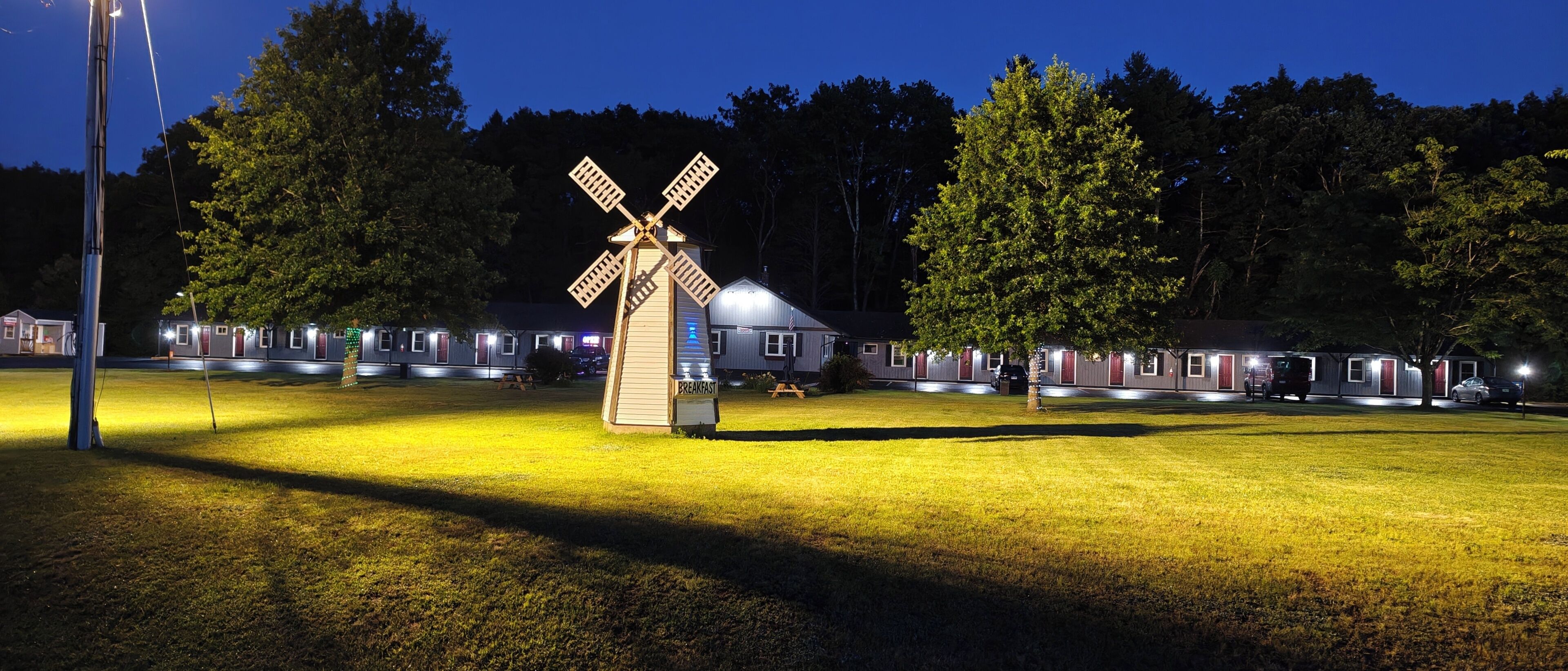A windmill, a row of cabins, and a grassy field at night.