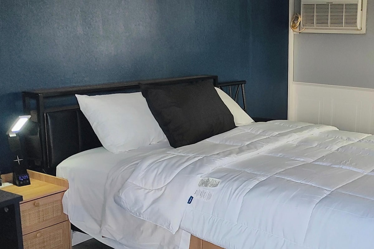 A neatly made bed with white bedding, a wooden headboard, and a bedside table with a lamp.