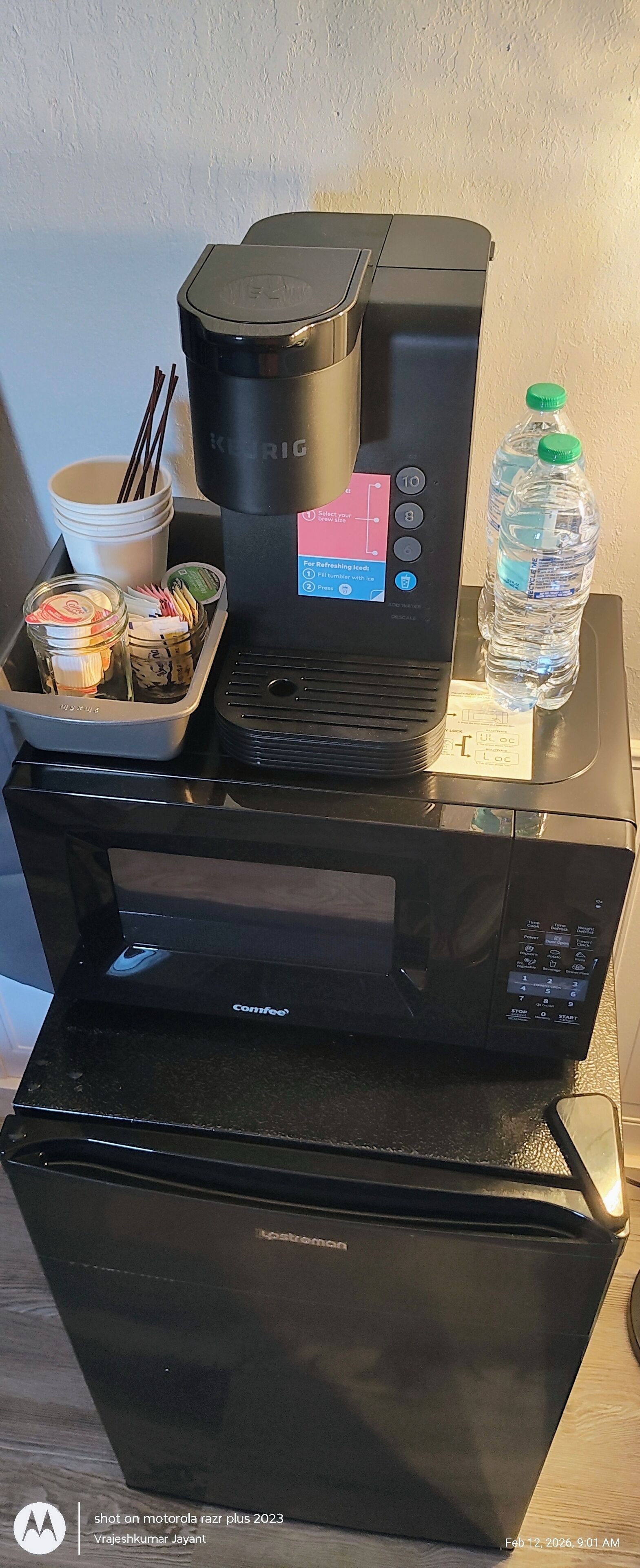 A coffee machine, a water bottle, a cup with chopsticks, and a tray with snacks on a counter.