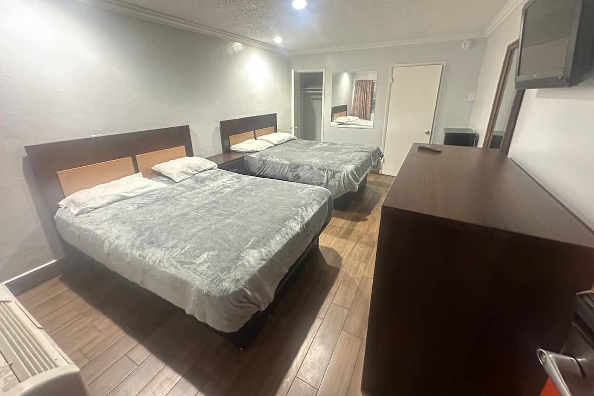 Una habitación de hotel con dos camas, piso de madera, un escritorio y un televisor.