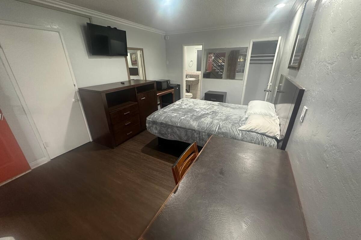 Un dormitorio con cama, cómoda, escritorio y televisor en la pared.