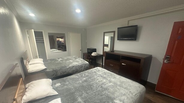 Ein Hotelzimmer mit zwei Betten, einem Schreibtisch, einem Fernseher und einem Kleiderschrank.