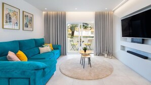 Ein modernes Wohnzimmer mit einem türkisfarbenen Sofa, einem runden Couchtisch und einem großen, an der Wand montierten Flachbildfernseher.