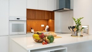 Eine moderne Küche mit weißen Schränken, einer Wand in Holzoptik, einem eingebauten Ofen und einer Arbeitsplatte mit Früchten und Küchenutensilien.